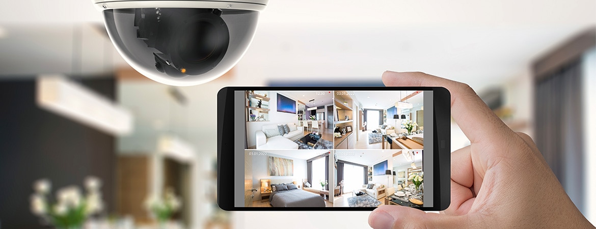 Person håller i en mobil med övervakningsbilder upp mot en övervakningskamera